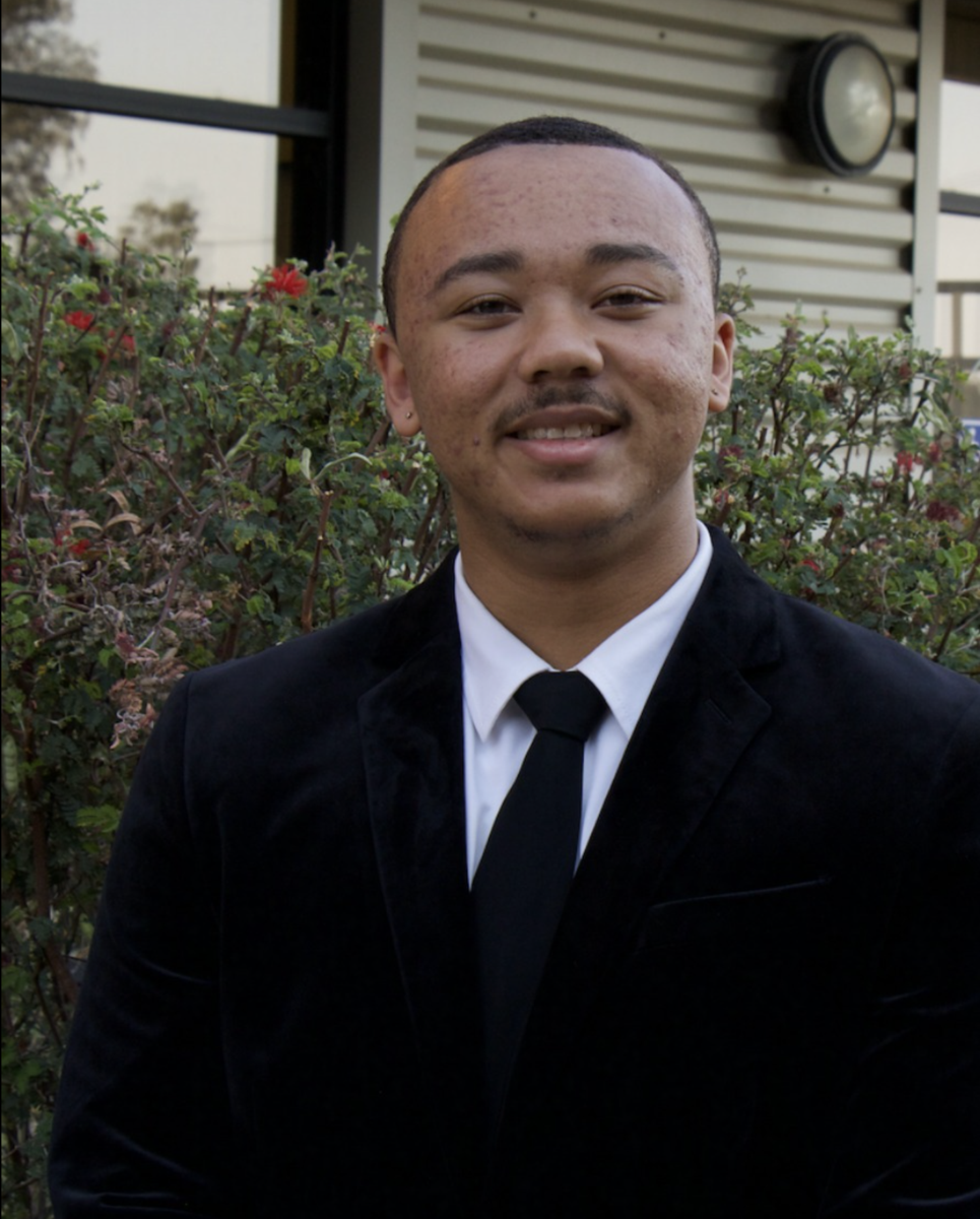 Kaiden Alderson in a black suit, with short cropped hair and a light mustache.