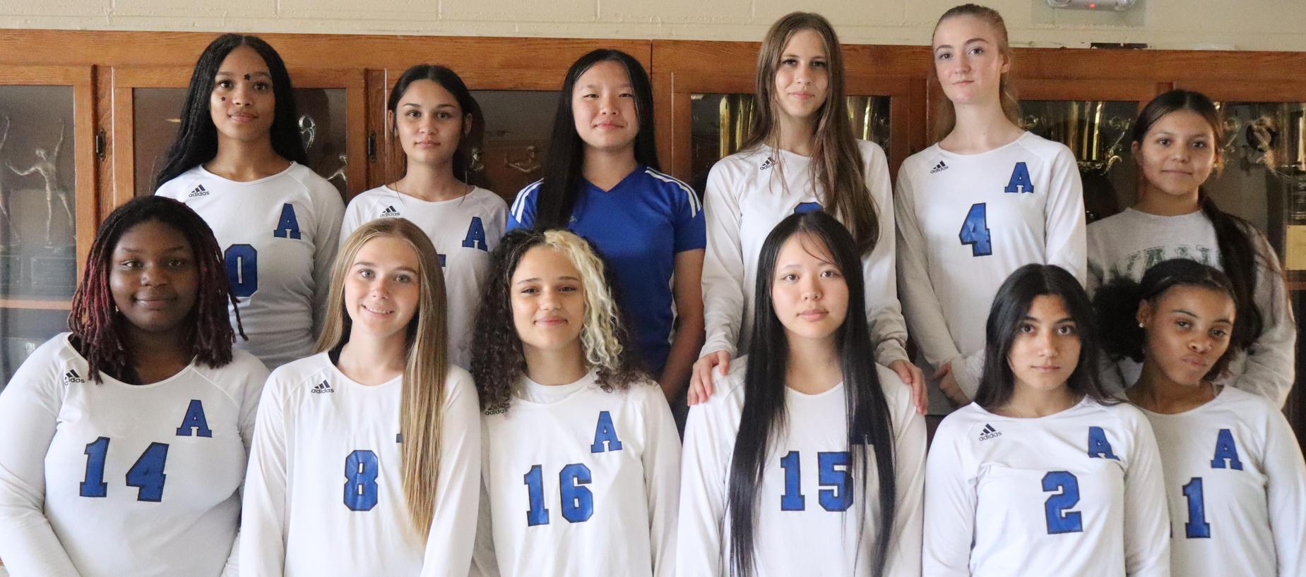 Group of volleyball players posing in white jerseys with blue numbers.