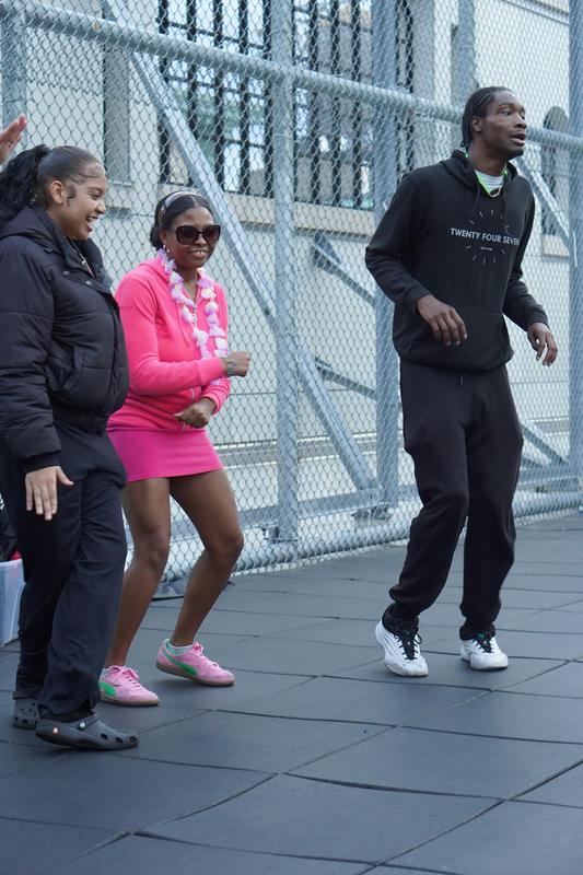 A pair of friends dancing, one wearing a pink outfit, in an energetic outdoor atmosphere.