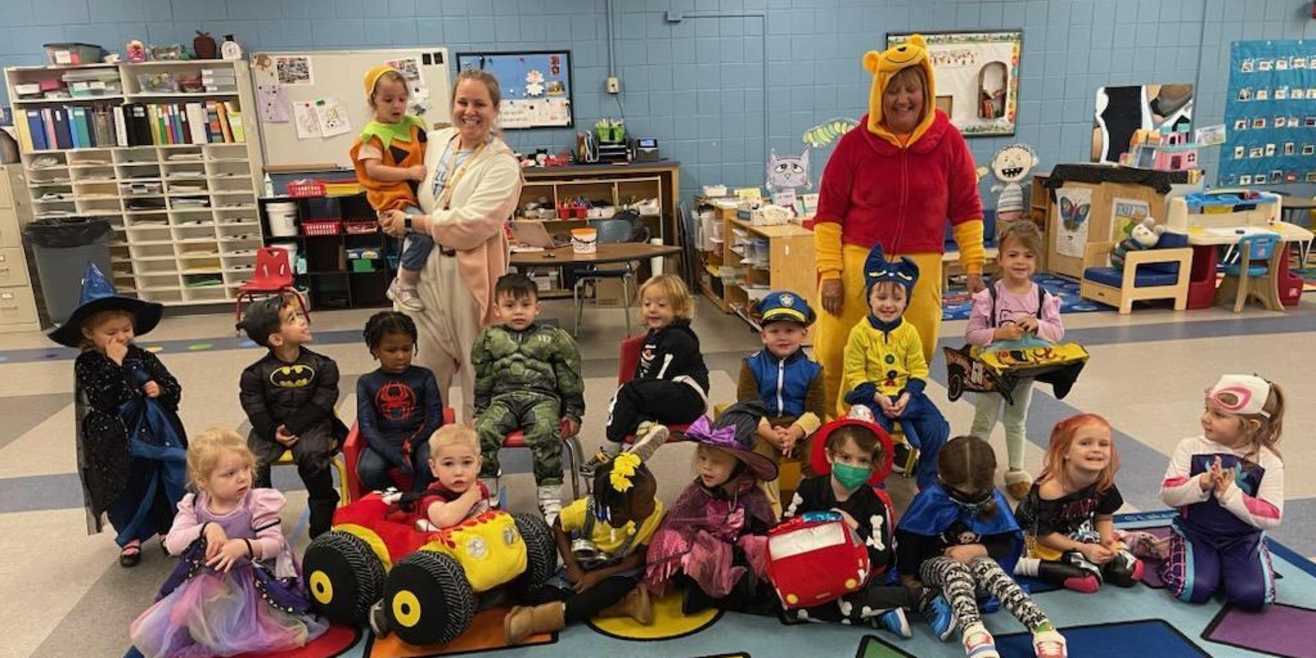Preschool students dressed up for Trick-O-Treat take a photo in their colorful classroom.