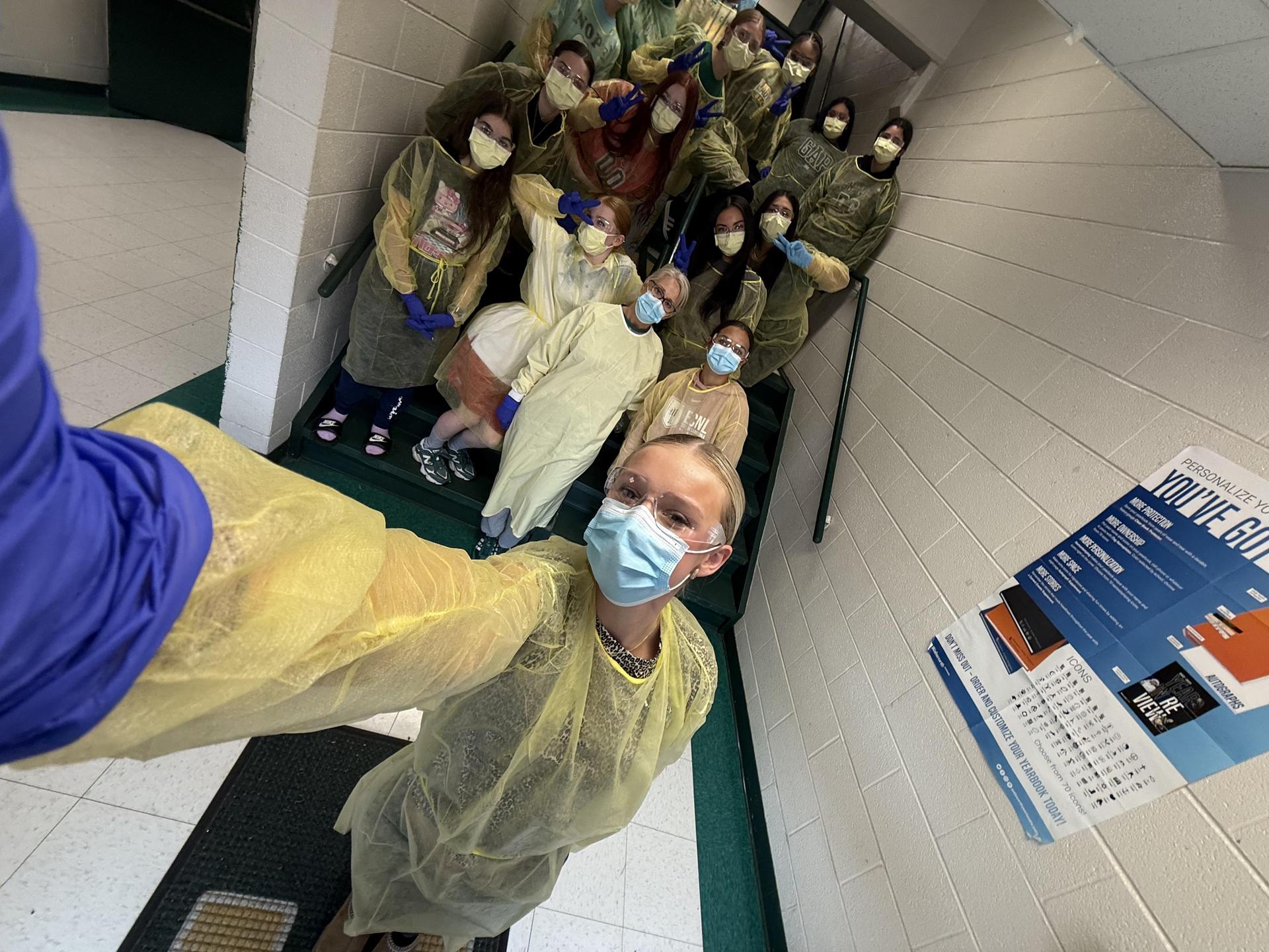 Group of students in yellow gowns posing on stairs with masks and gloves.