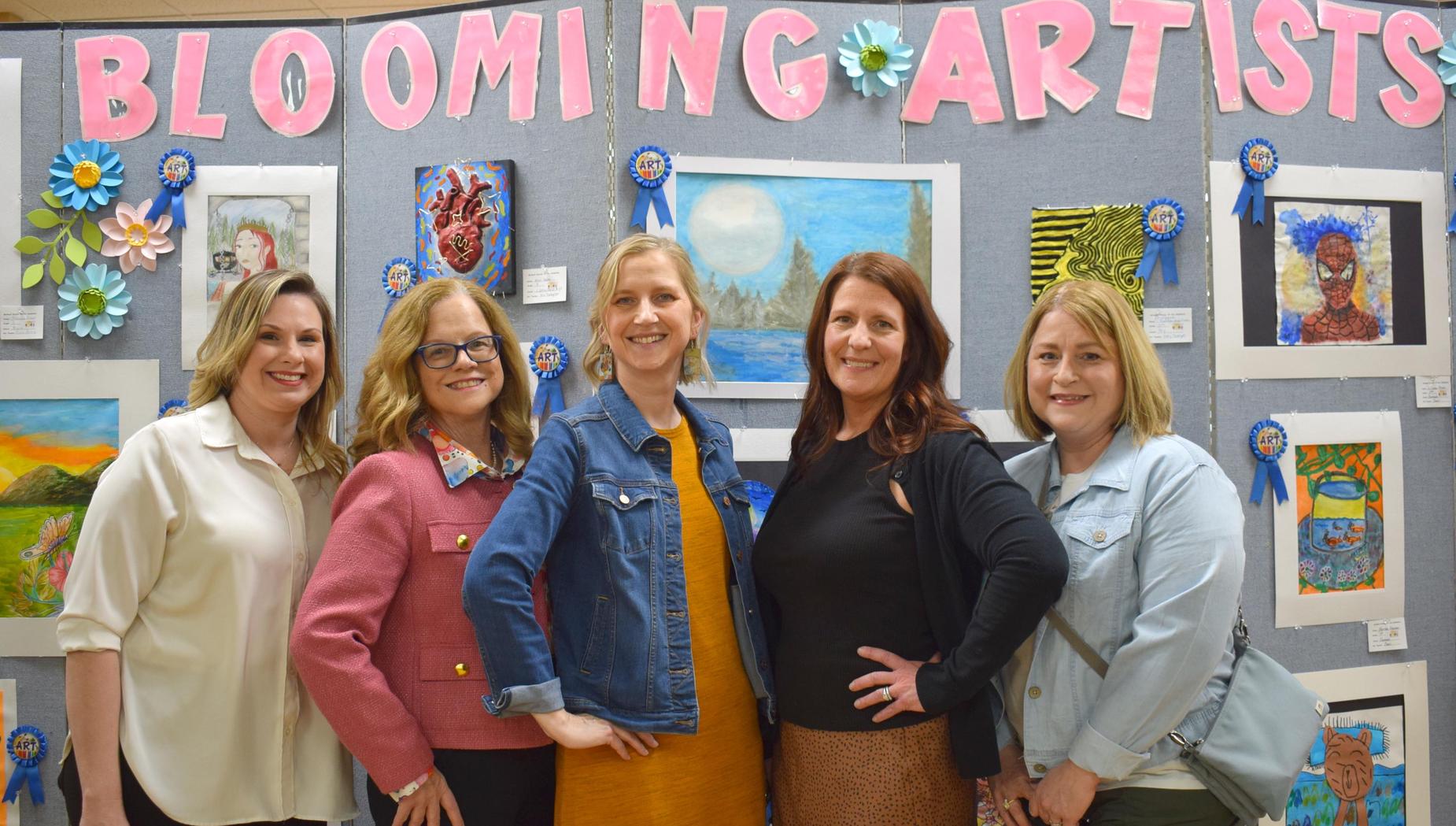 Five women posing in front of an art display with ribbons and decorations.
