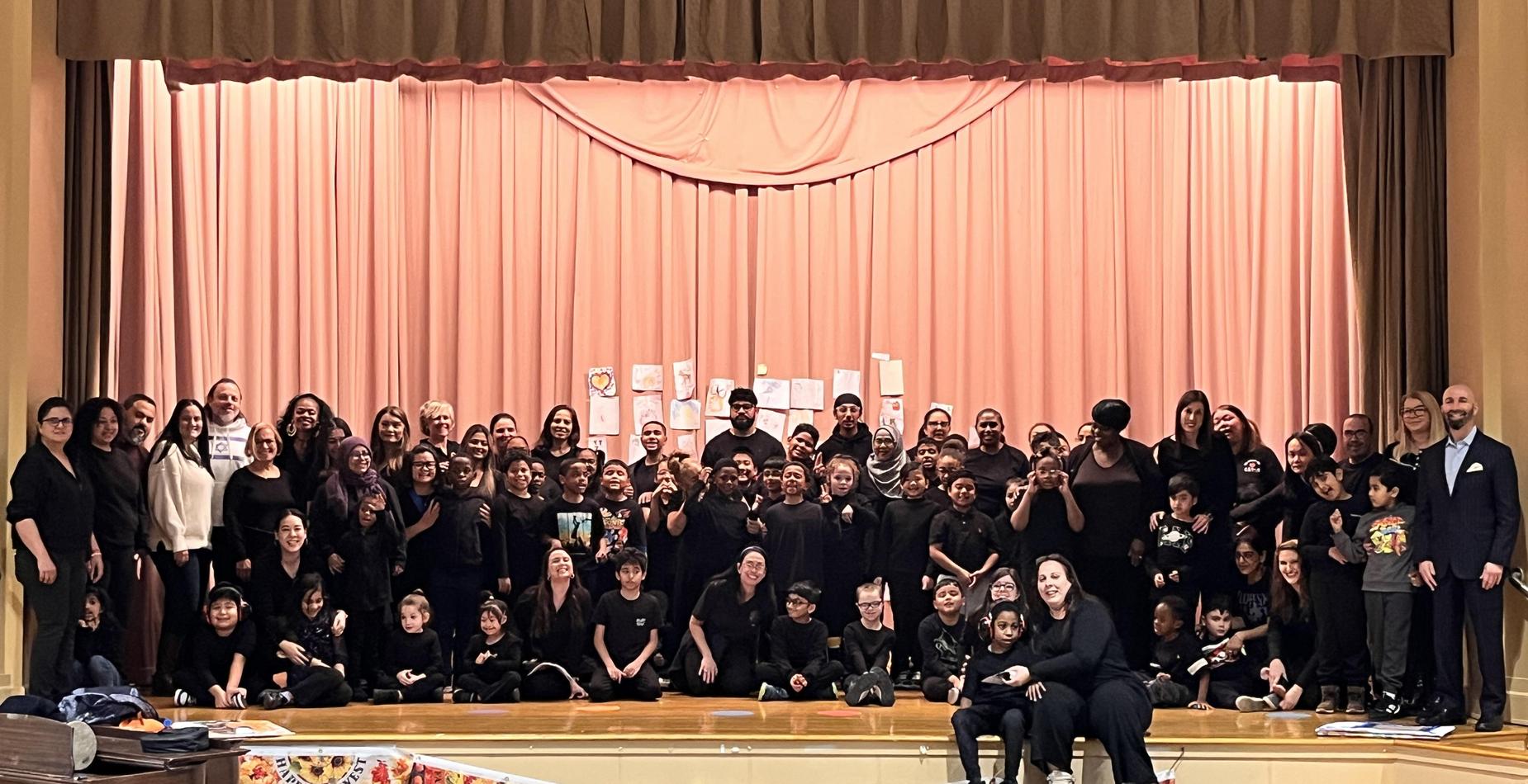 Big group of individuals in black outfits on a stage with a curtain.