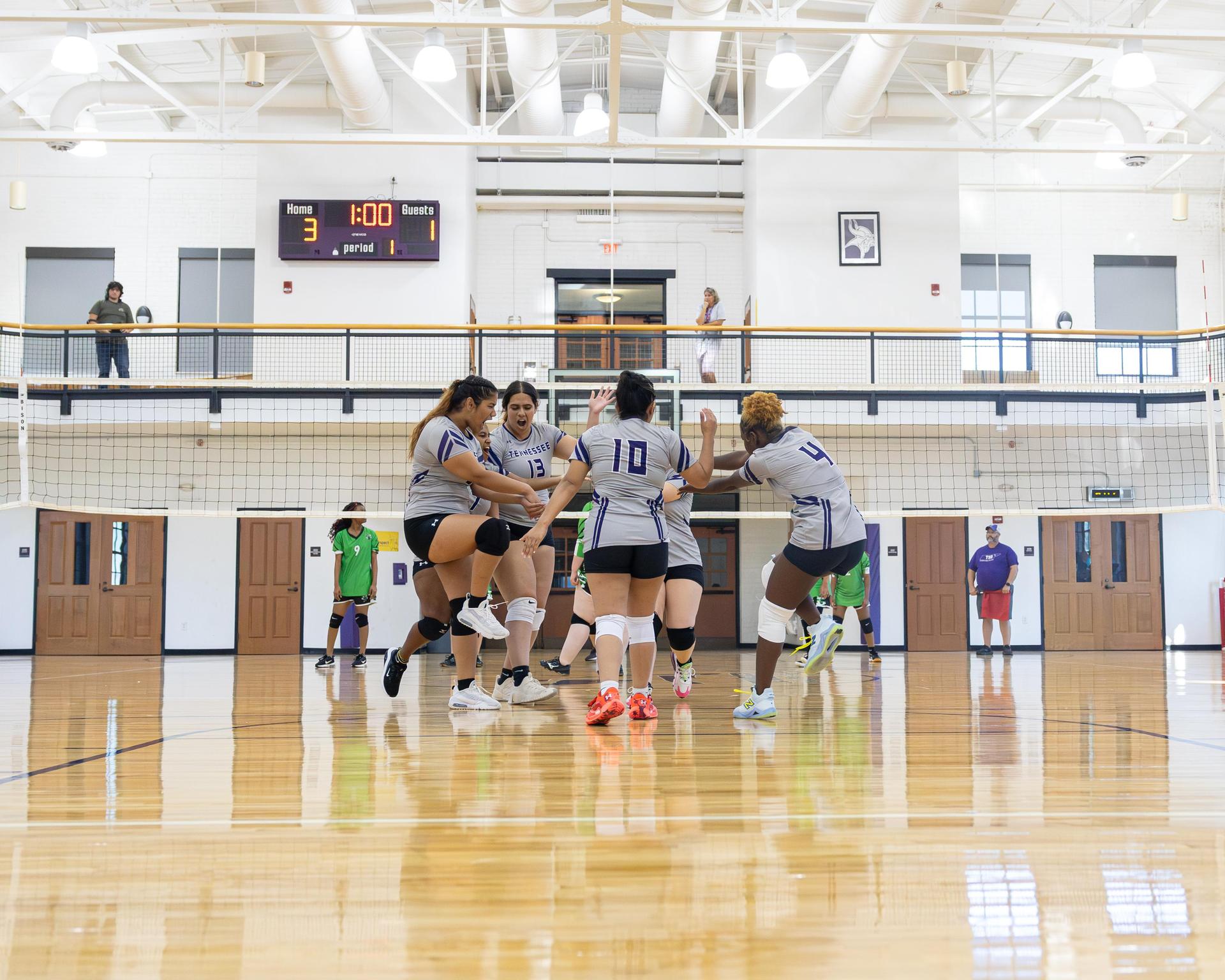 Players celebrating a point during a volleyball game in a gymnasium.