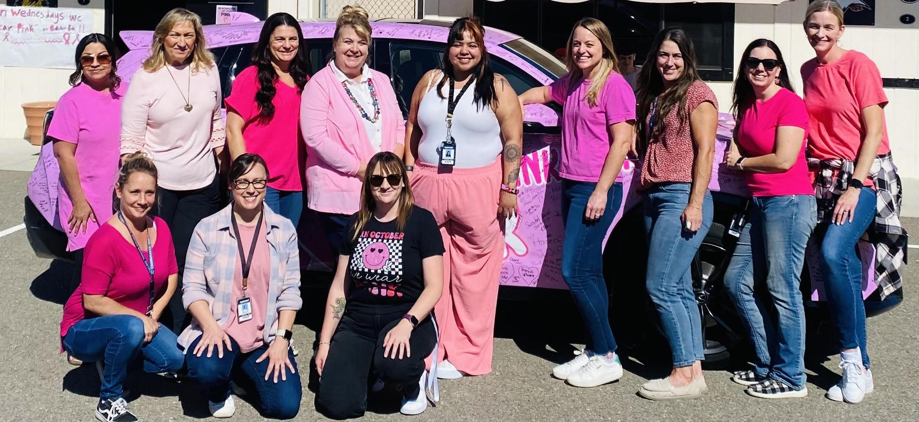 Group of women in pink clothing posing beside a decorated car outside.