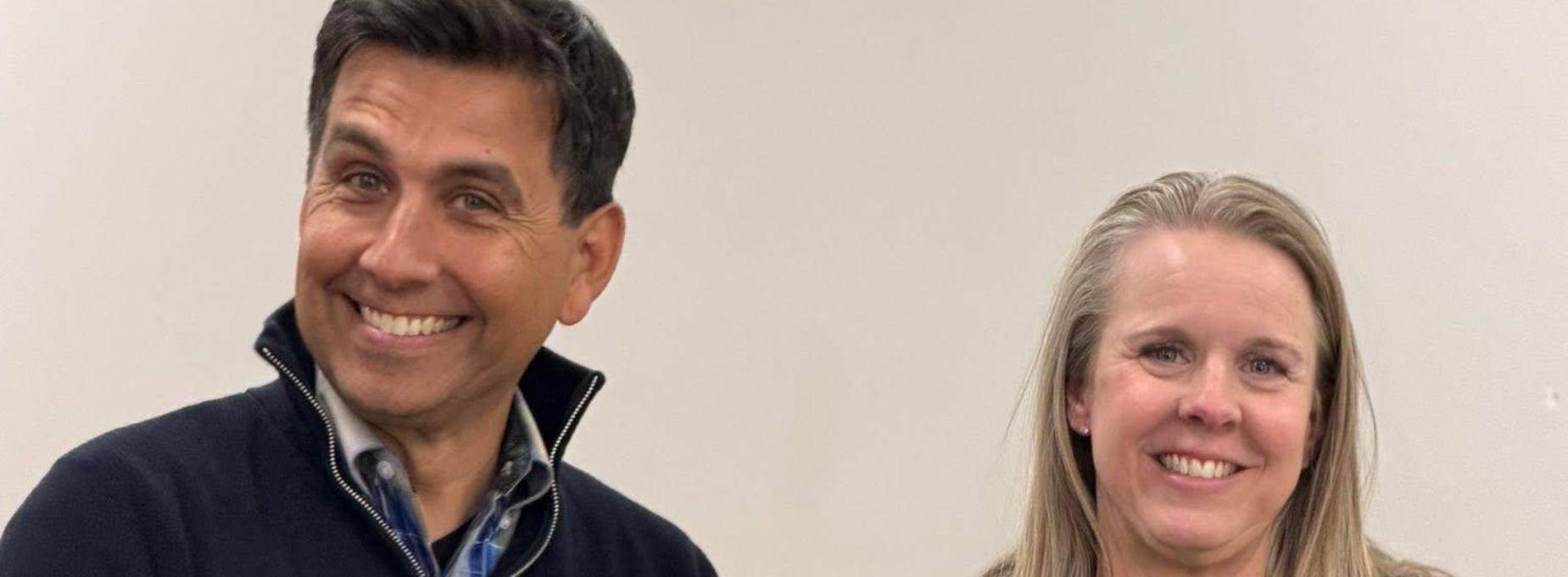 Two smiling individuals posing for a photo against a plain background.