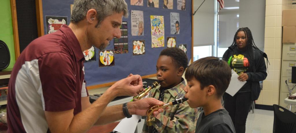 teacher instructs two boys how to blow into a saxophone mouthpiece