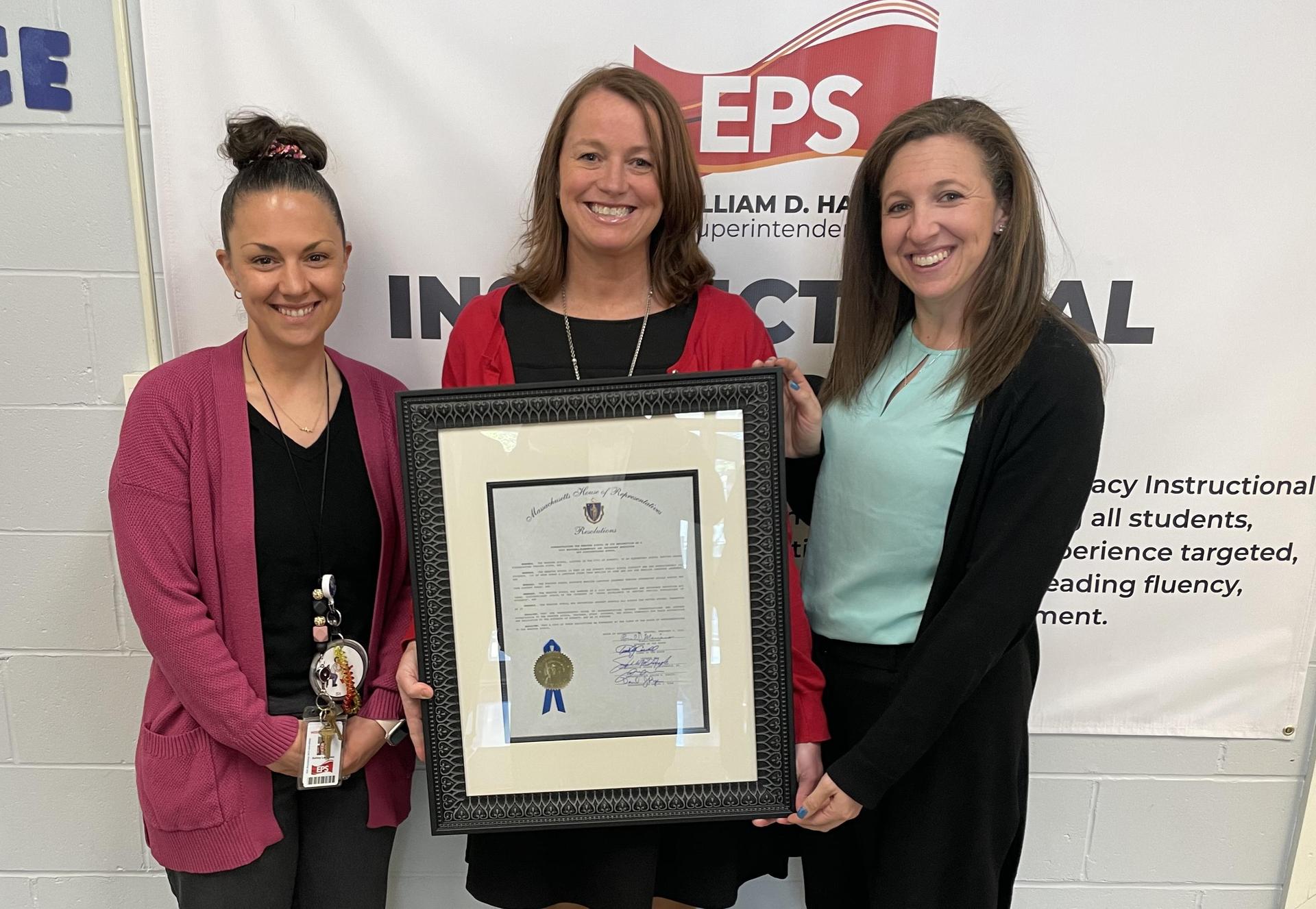 Three teachers holding a formal, framed prclomation