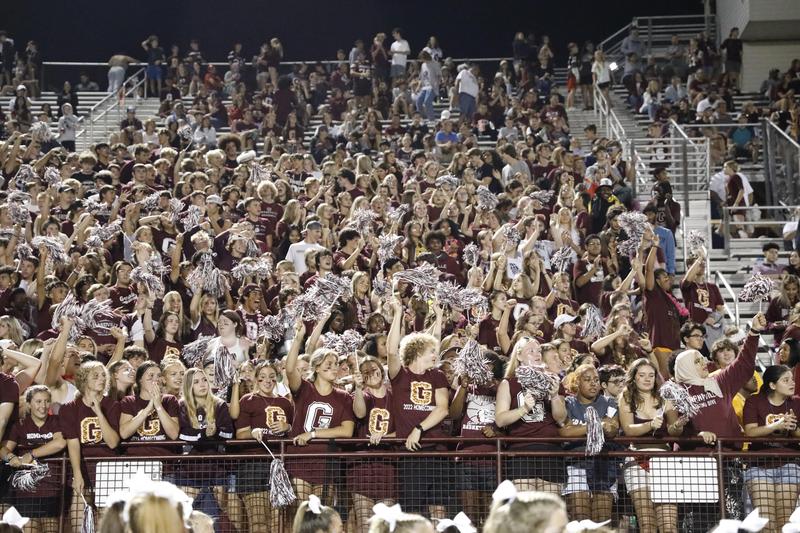 fans in the stands at the game wearing maroon shirts and waving pom poms