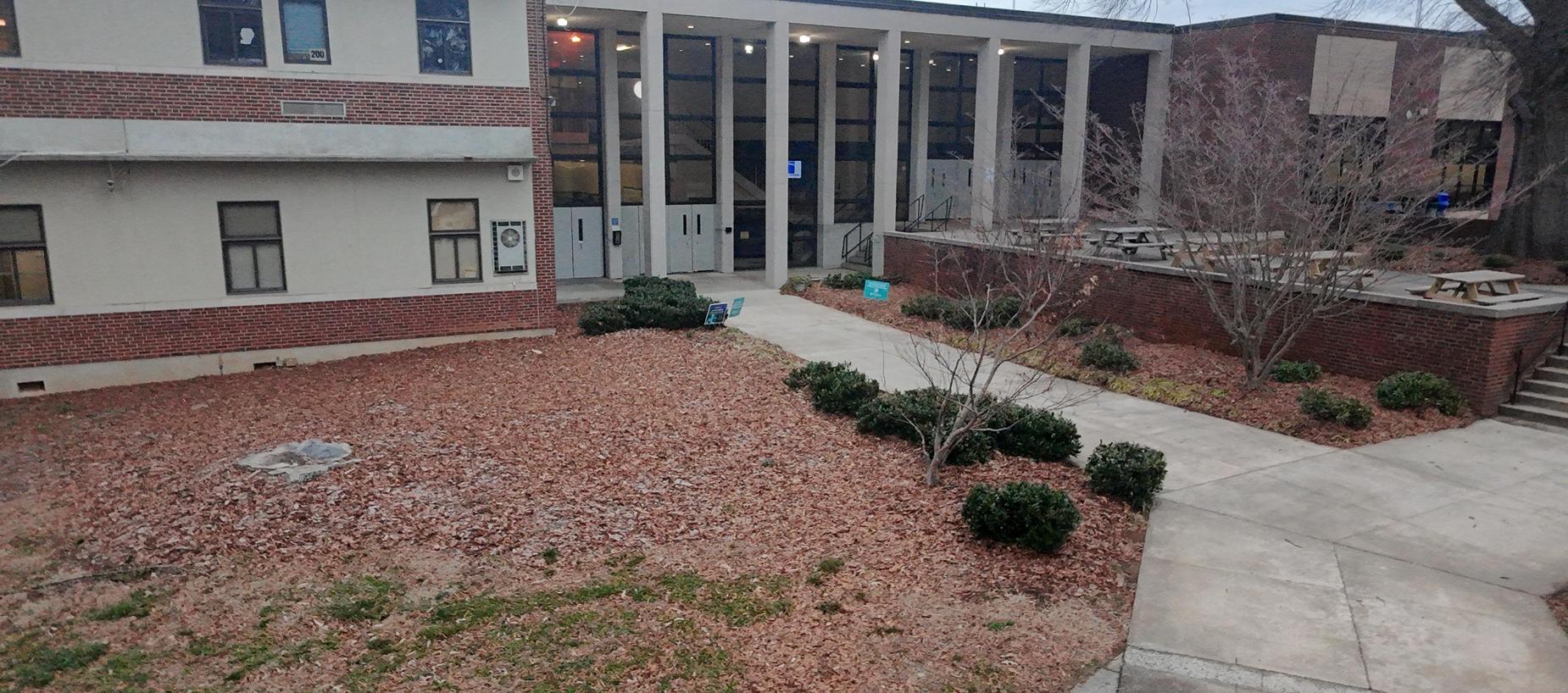 A school courtyard with pathways, bushes, and brick buildings.