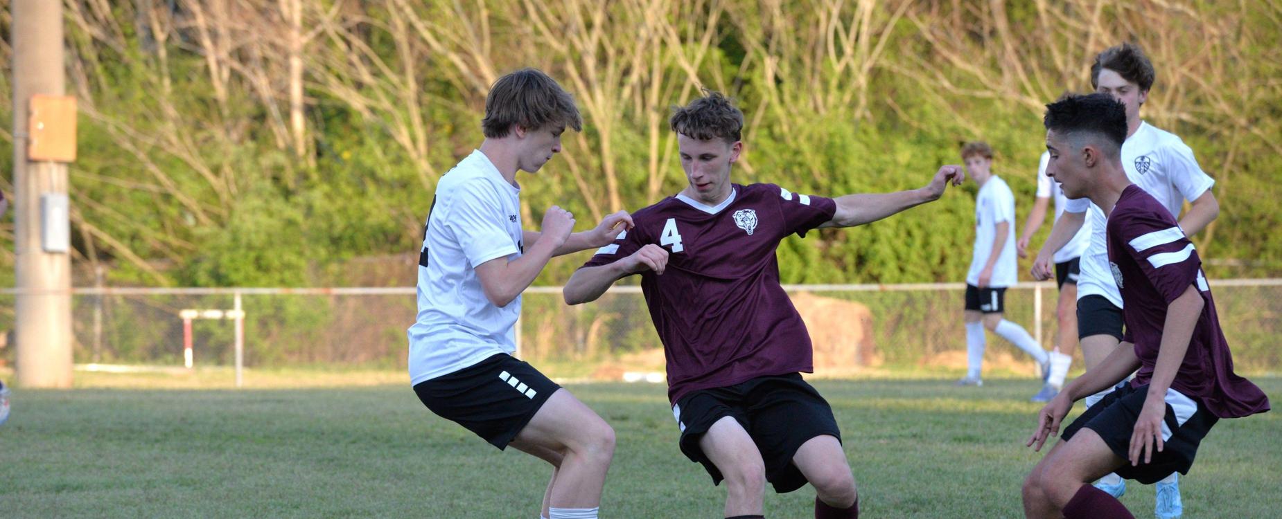 Two soccer players in maroon and white uniforms competing for the ball on a field.