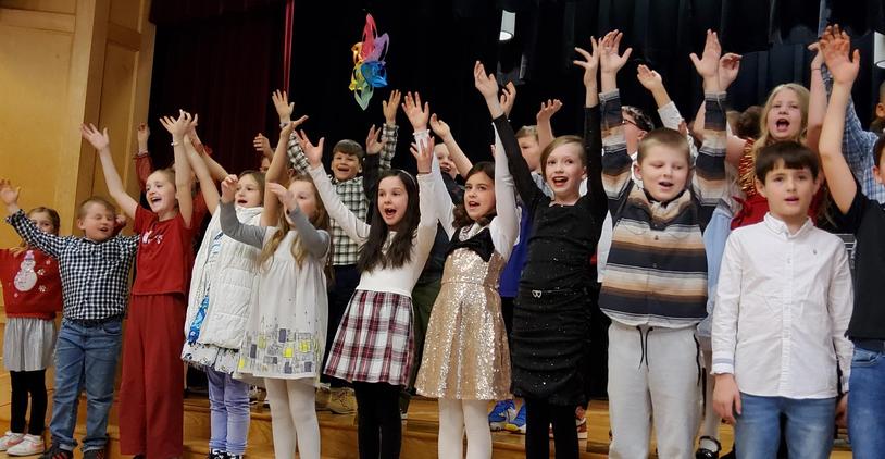 Children joyfully performing on stage with hands raised.