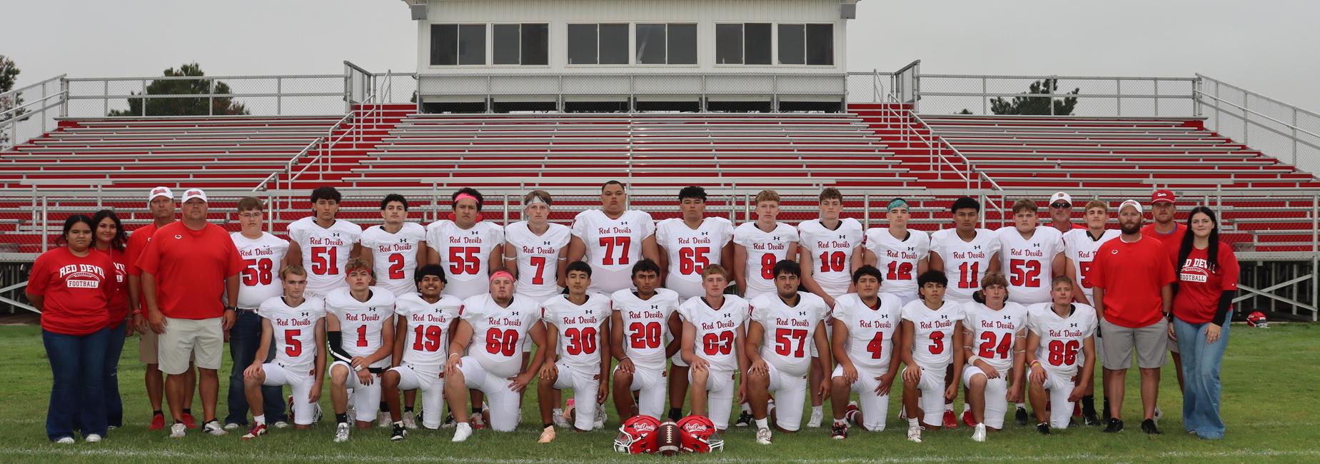 Large team of football players in white uniforms with red accents, posing on a field.