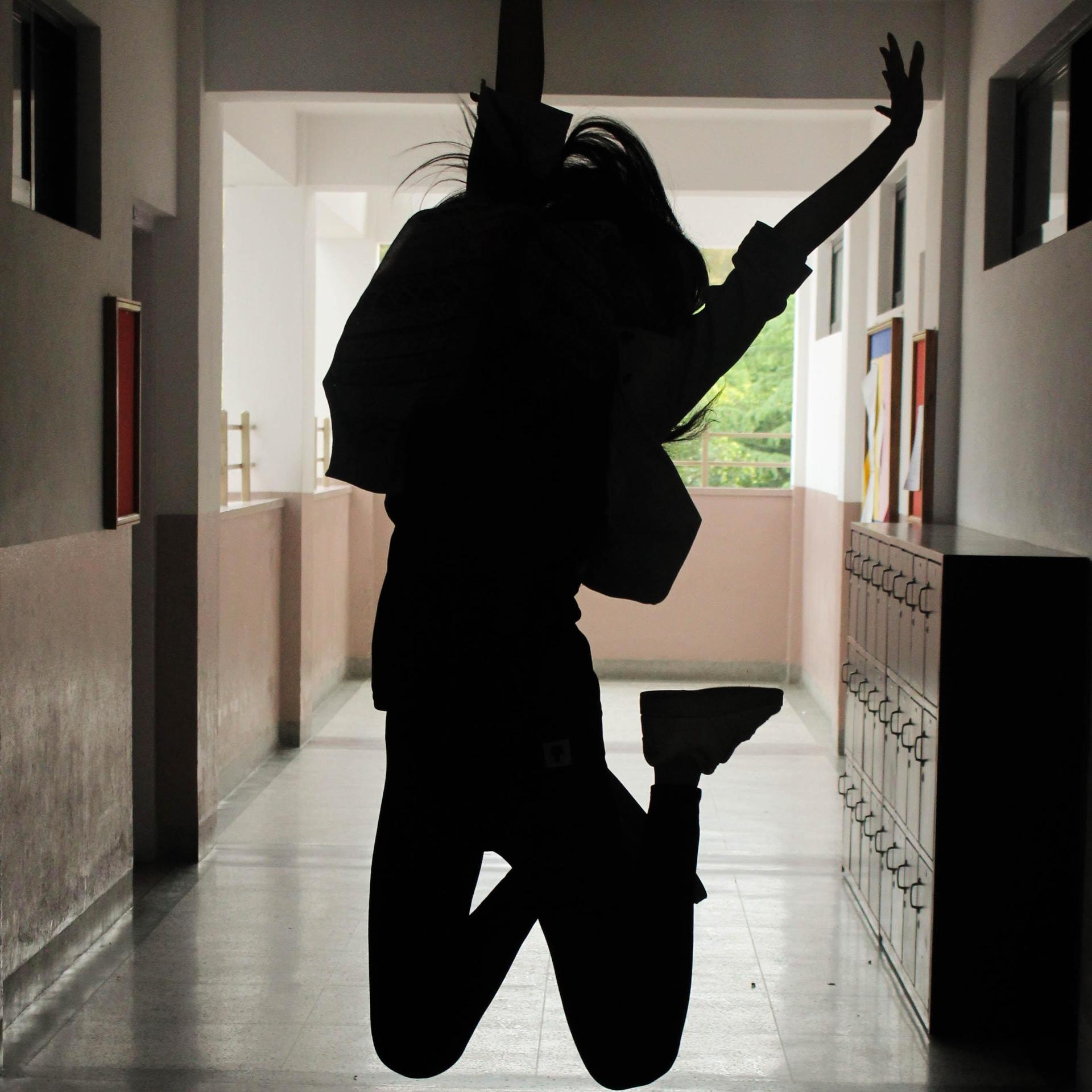 A silhouetted figure jumping in a corridor with lockers and open space behind.