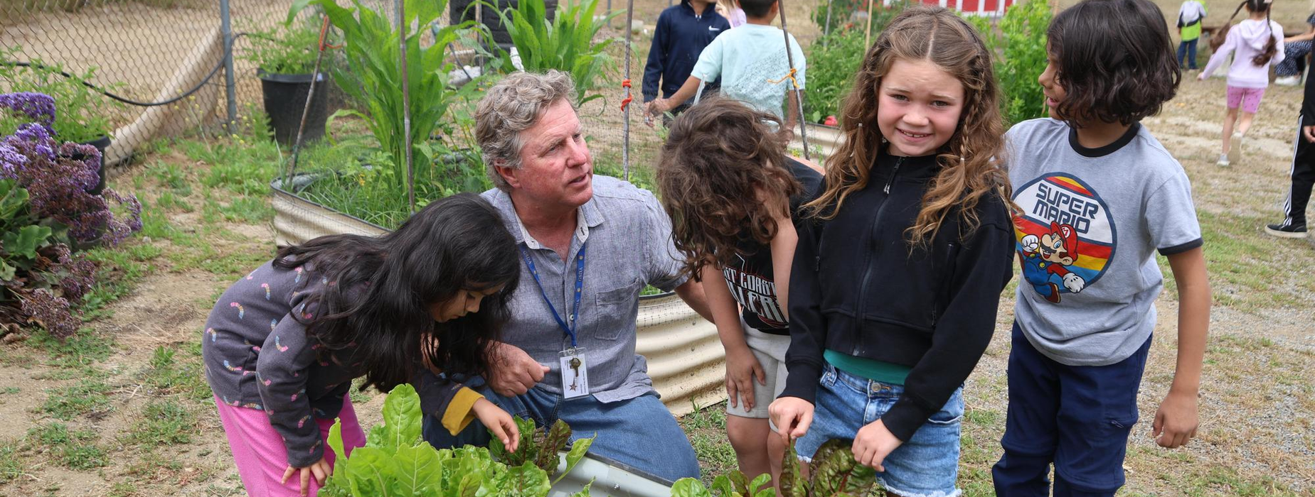 Group of children and a man gardening together with plants.