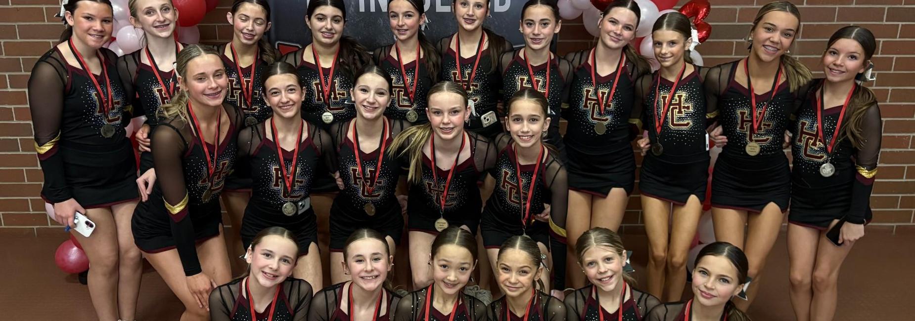 A group of cheerleaders in black uniforms with medals and red ribbons posing together.
