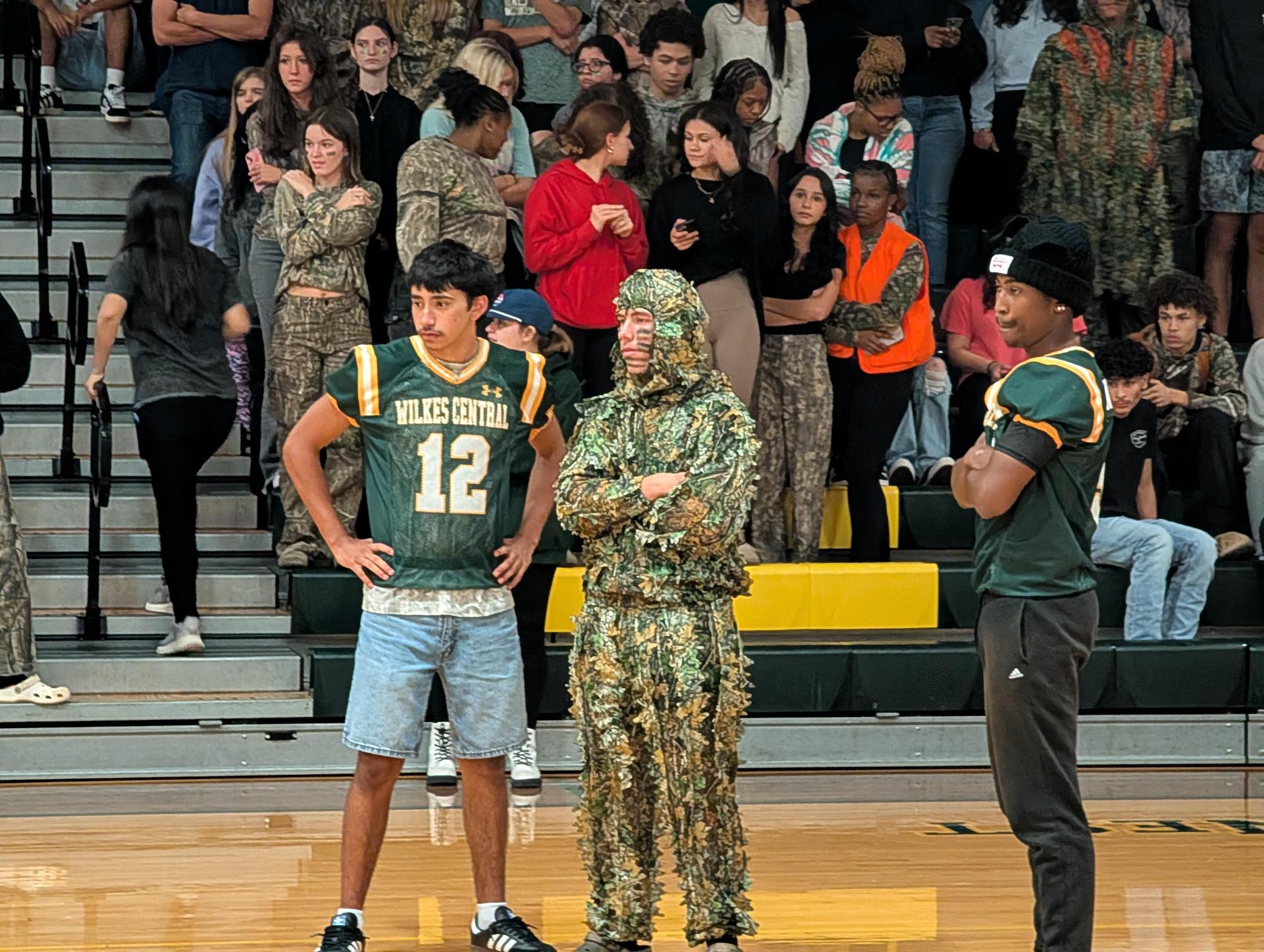 Students in various outfits, including camouflage and jerseys, gather in a bleacher area.