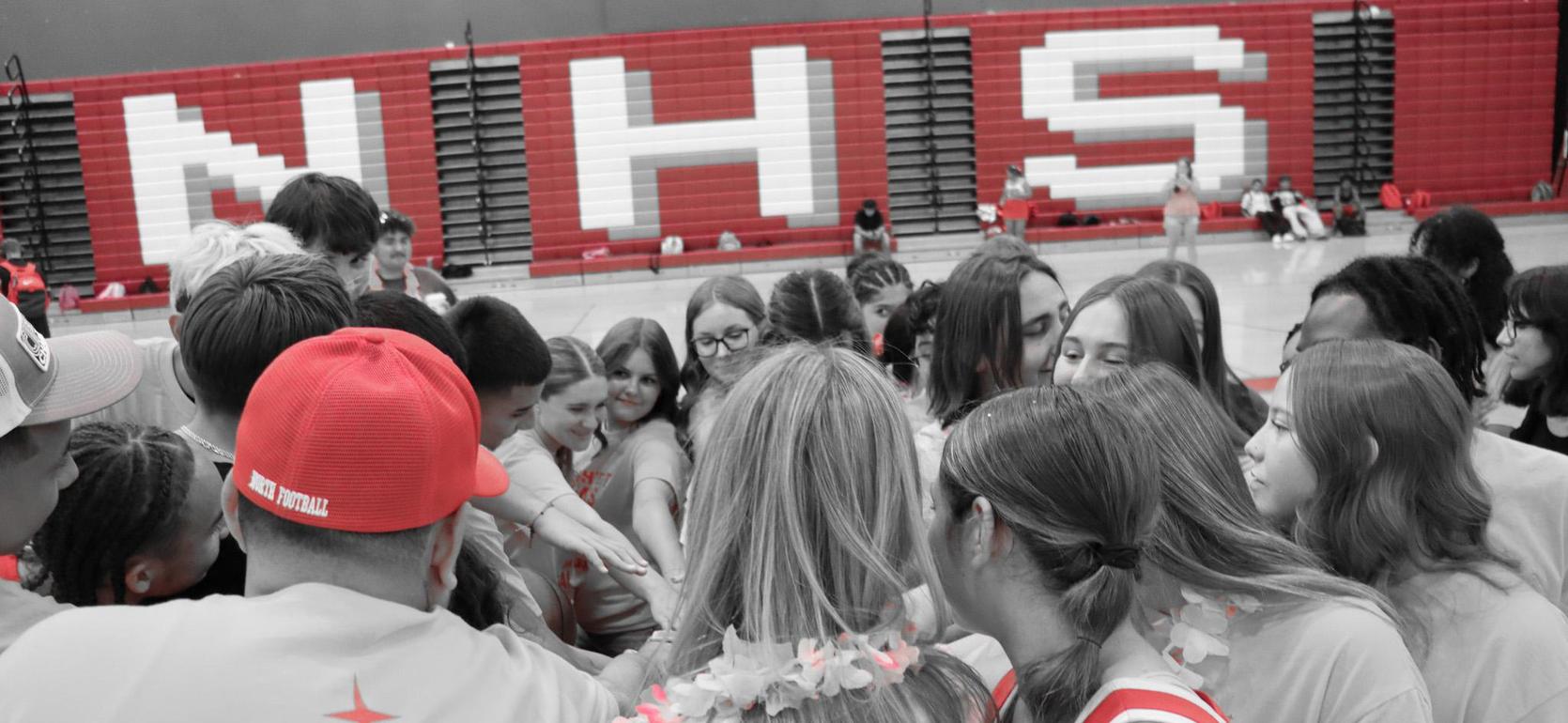 A diverse group of students huddled together, showing unity and excitement in a gymnasium.