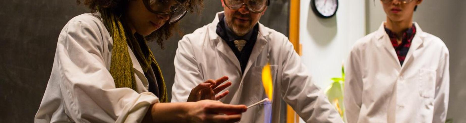 Girl student and teacher watching colorful flame from bunsen burner