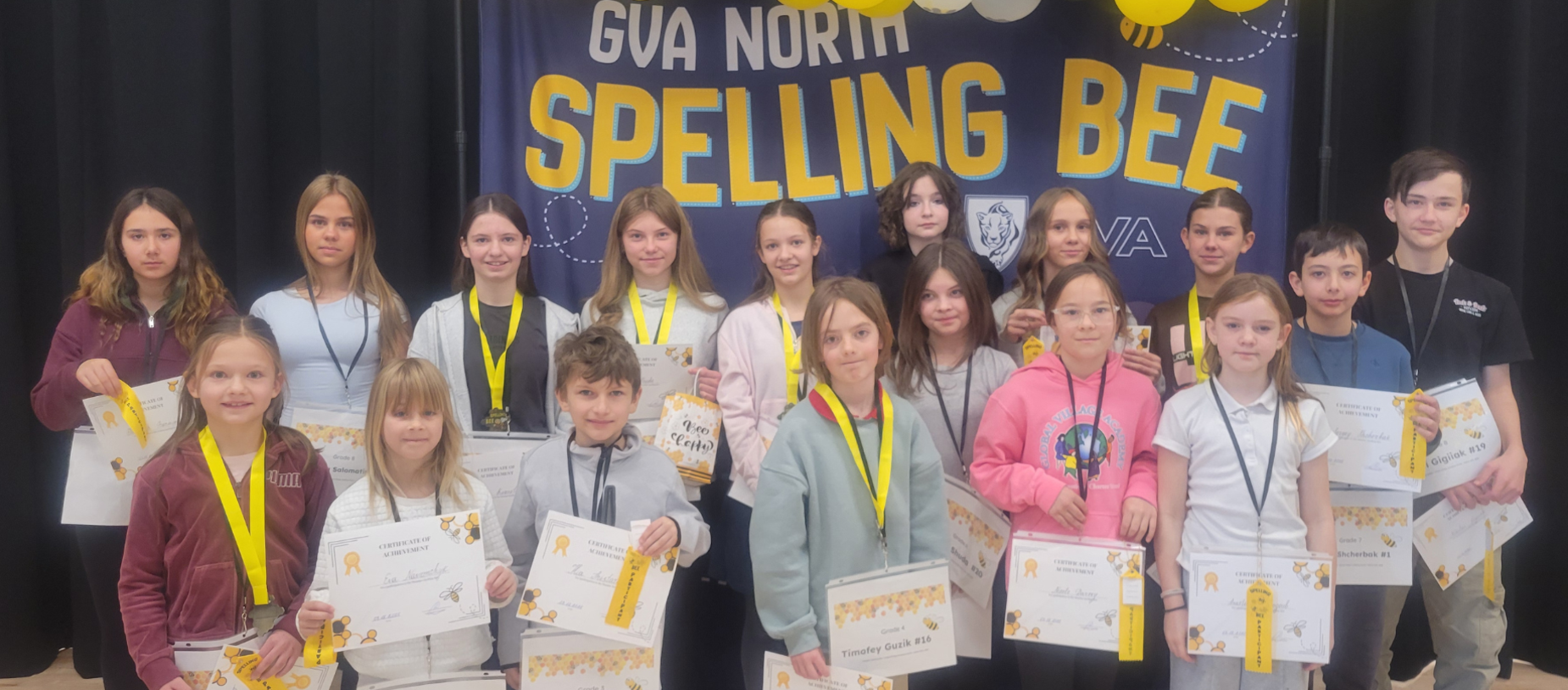 Students posing at a spelling bee event, holding certificates and awards.