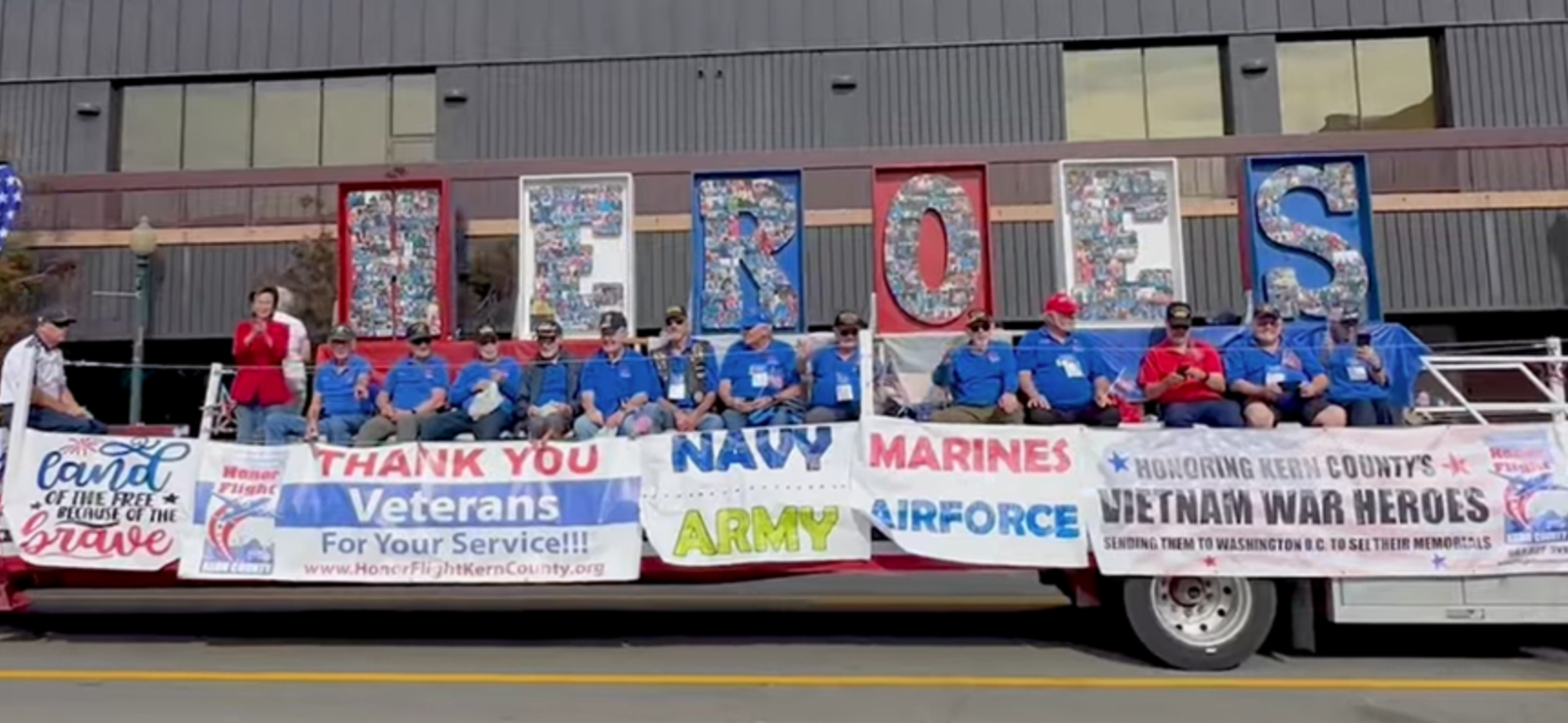 A parade float with veterans in blue shirts, honoring military heroes with large letters spelling 'HEROES'.