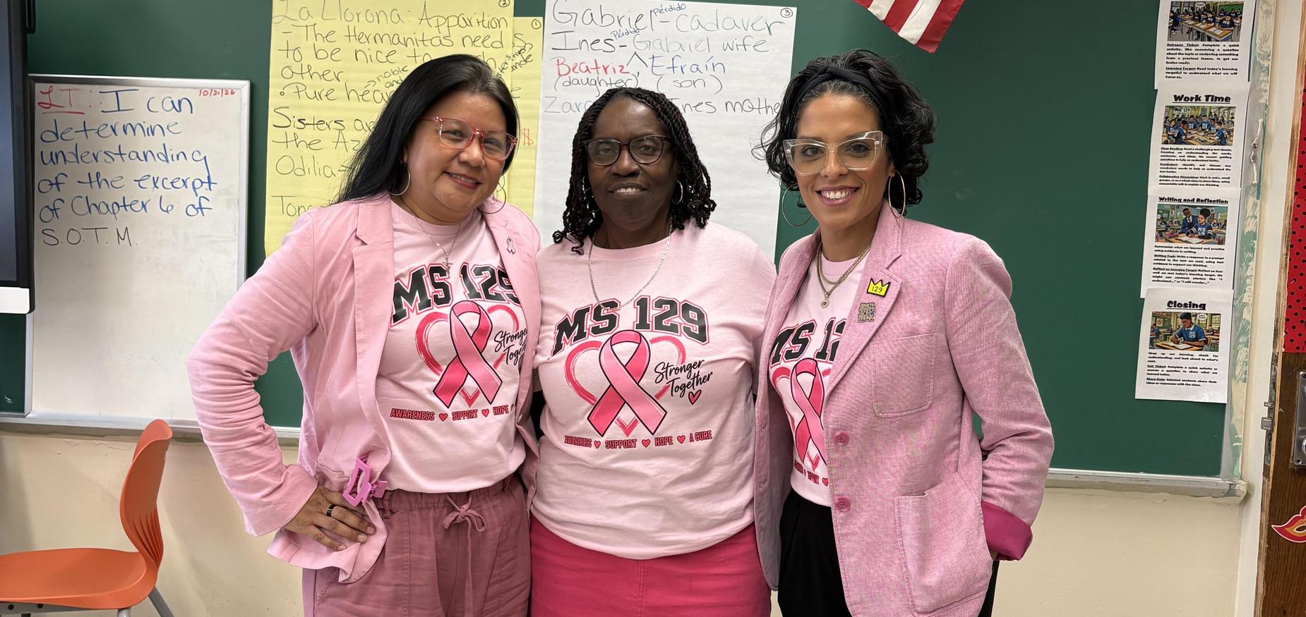 Three people dressed in pink standing in a classroom