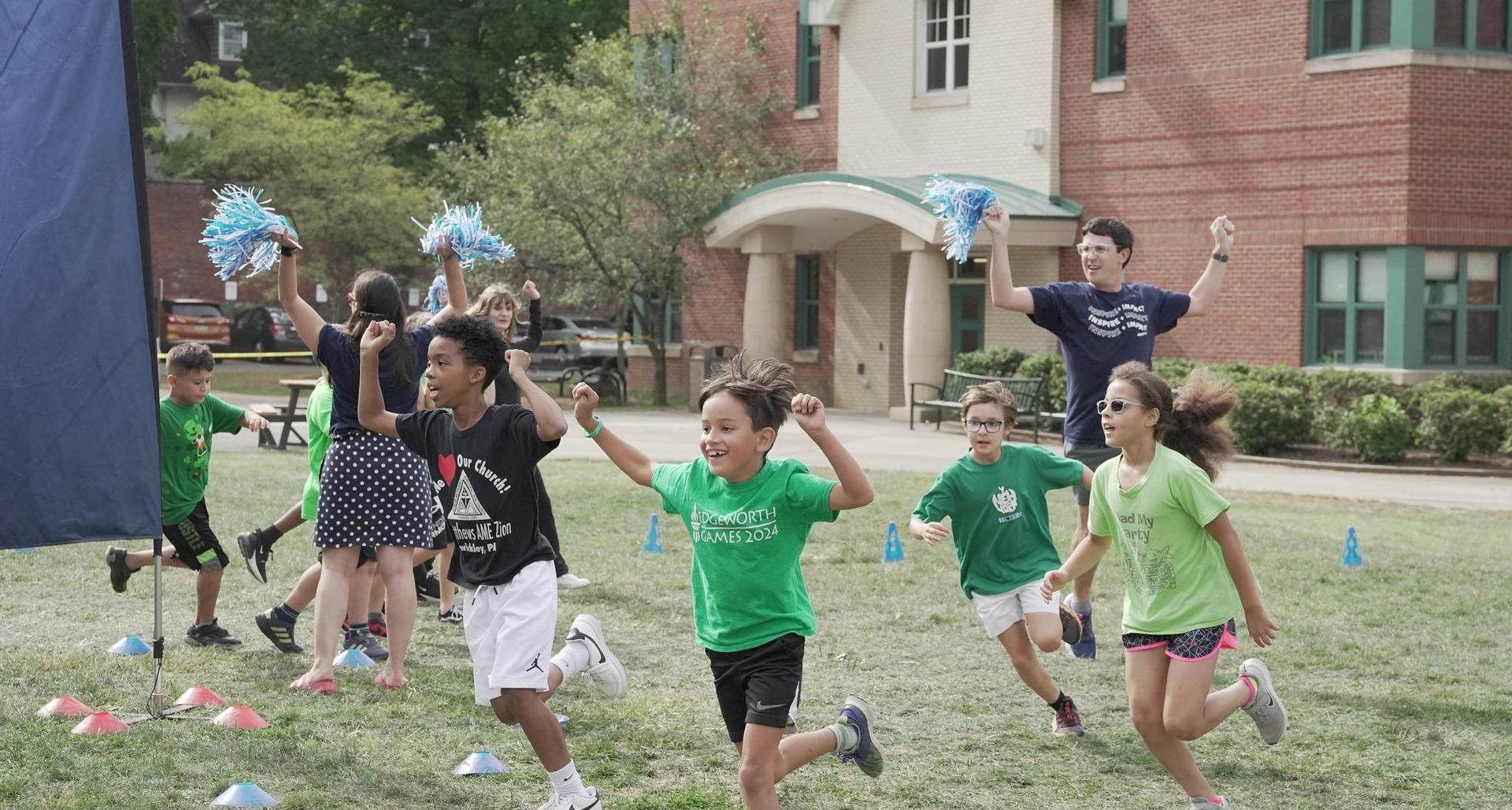 Children running on a grassy field while cheering with pom-poms.