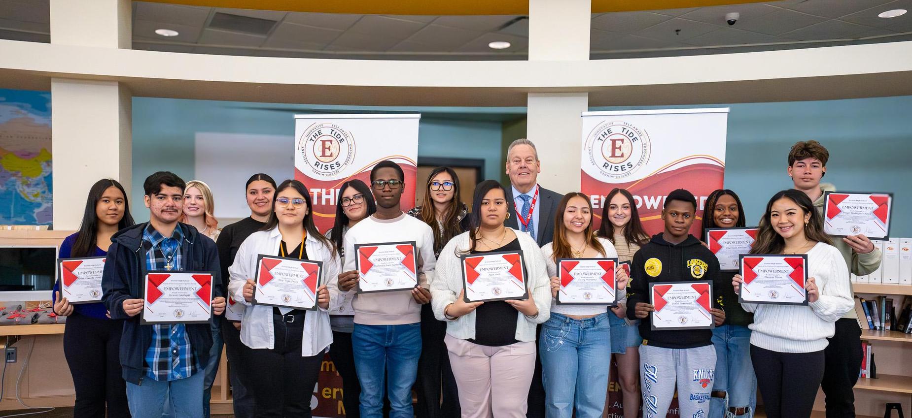 Group of students holding certificates, standing with a man in a suit.