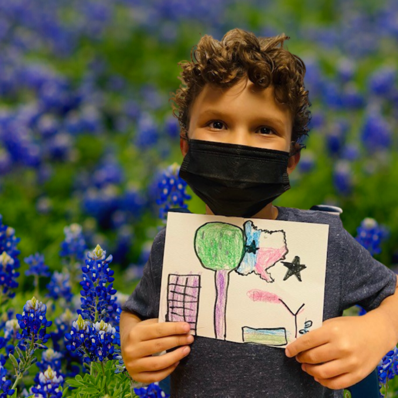 boy holding his artwork in front of bluebonnets
