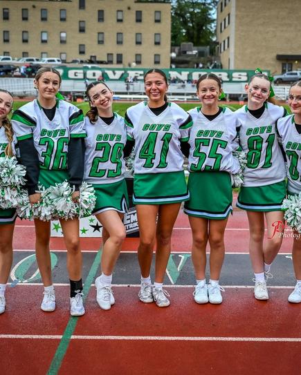 Cheerleaders in green and white uniforms posing together on a sports field.