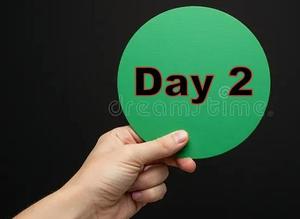 Single hand holding a green circular sign saying "Day 2".