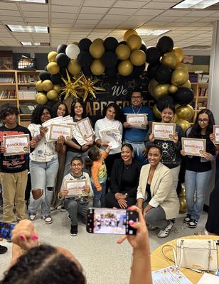Group of people holding certificates in front of a celebratory balloon display.