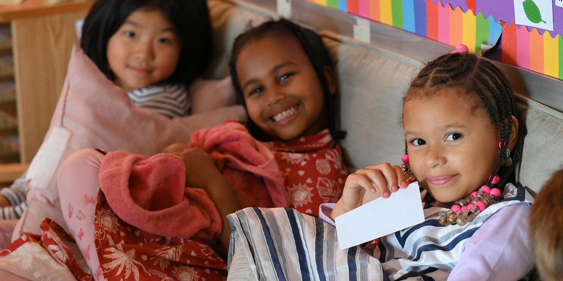 Three girls sitting together on a couch, smiling and holding cards.