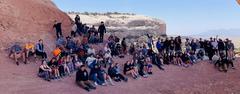 A large group of people gathered under a natural rock arch in a scenic outdoor area.