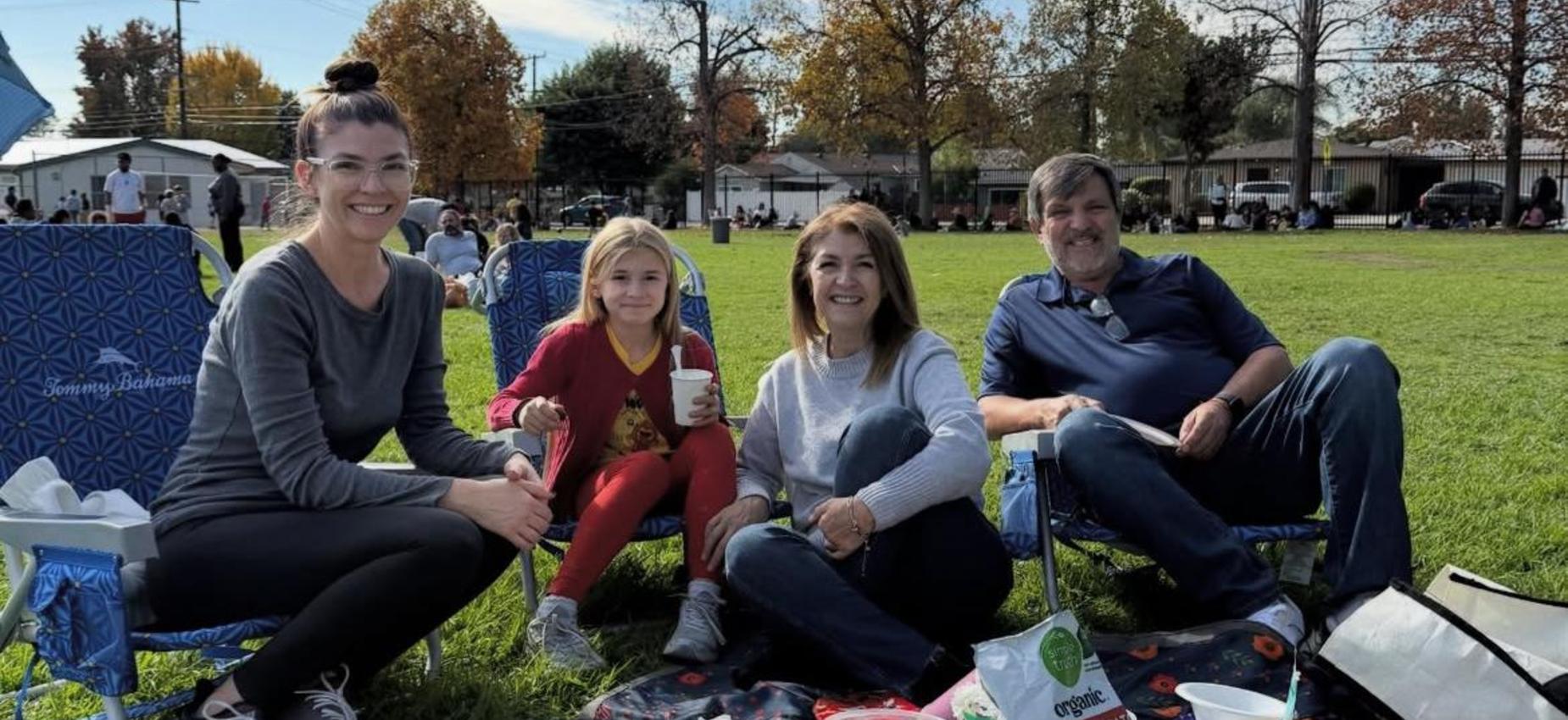 Four people sitting on lawn chairs at a park, enjoying a sunny day together.