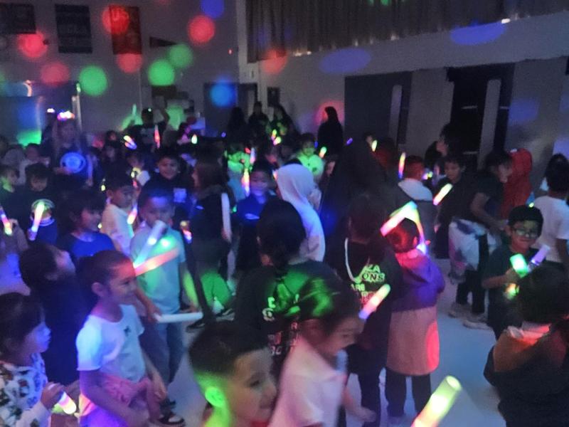 A lively group of children dancing with glow sticks in a colorful party setting.