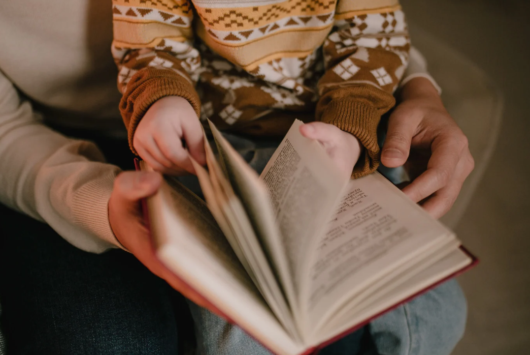 A child and adult reading a book together, focusing on the pages.
