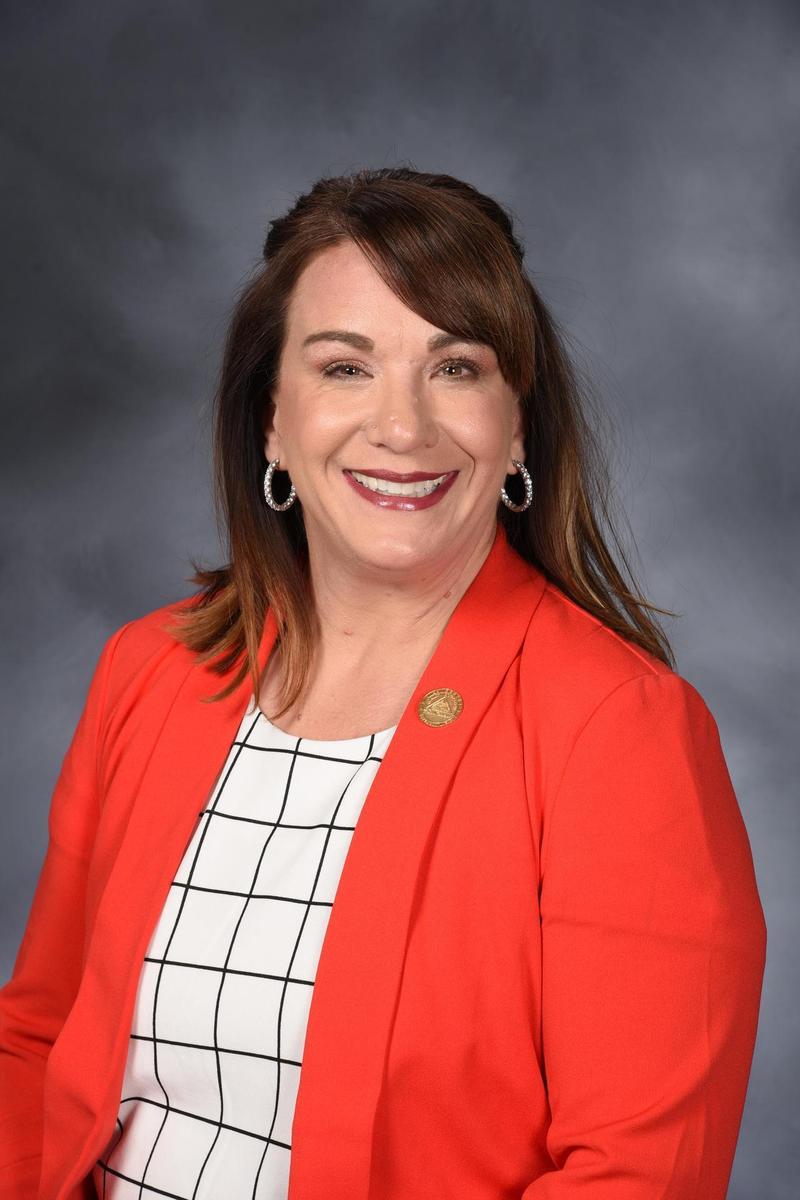 Williamson with dark brown shoulder length hair and a bright red suit jacket