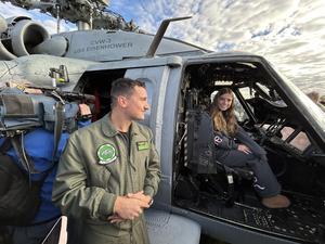 Image of a female student sitting in the chopper talking to the pilot who is standing outside the chopper