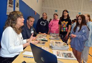Two adults talk to students while displaying newspapers at a table.