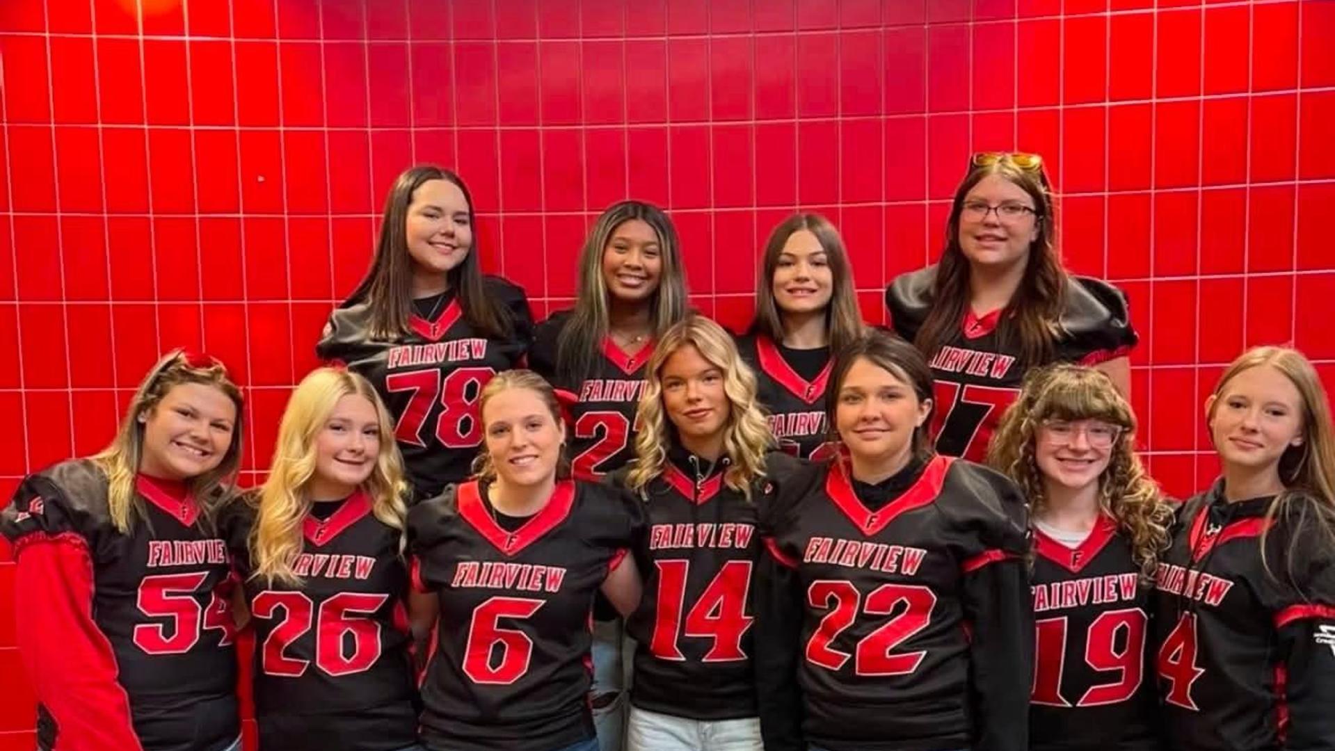 Group of girls in football jerseys posing together, smiling for the photo.