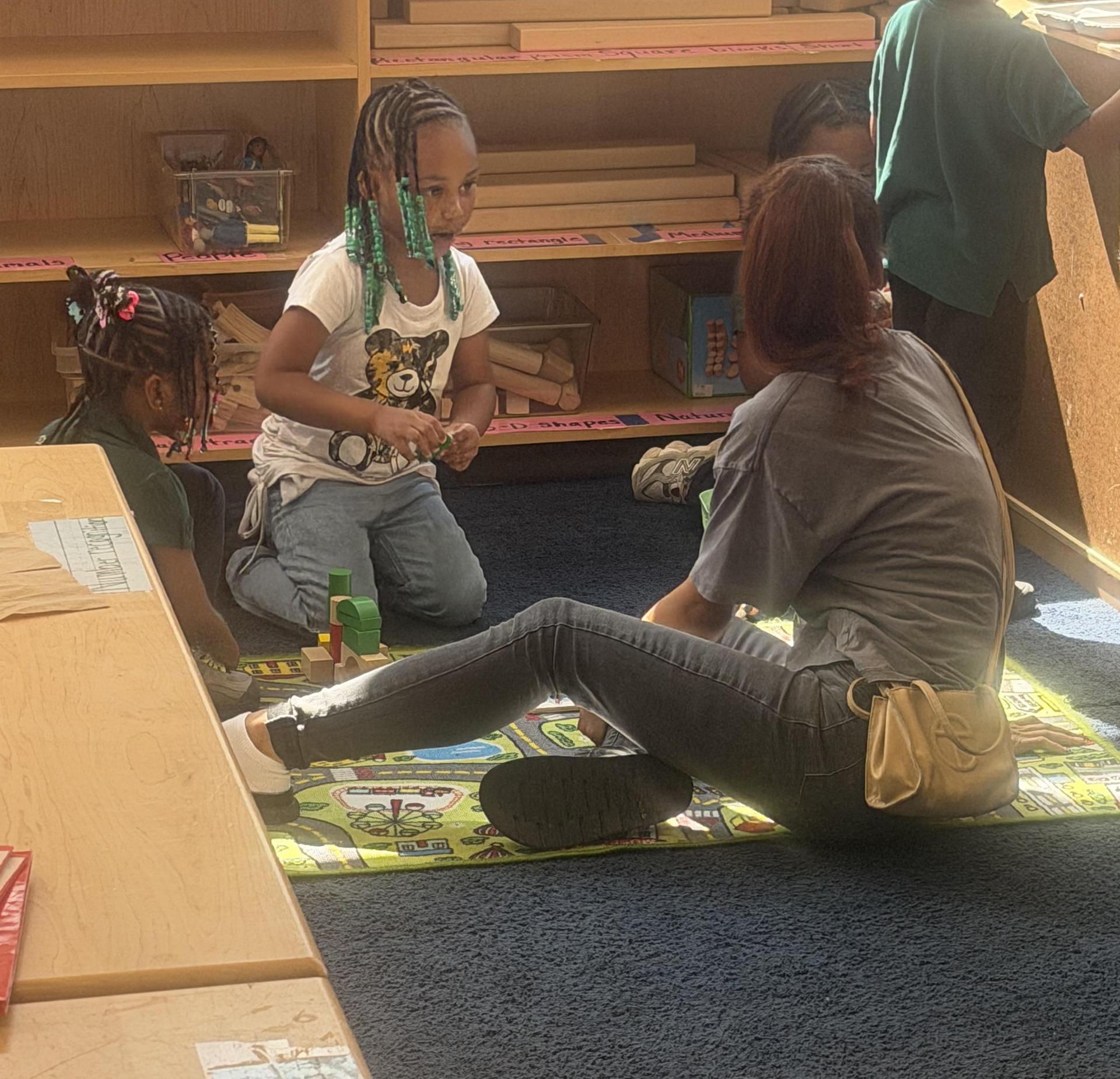 Children playing with blocks on a colorful mat in a classroom setting.