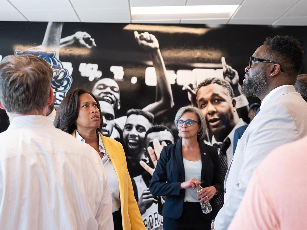 A group of people stands inside, observing a wall mural of diverse individuals cheering.