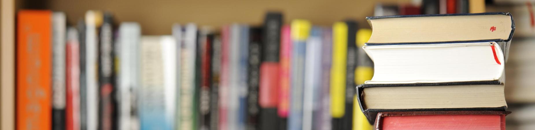 Stack of books in the foreground with a blurred bookshelf behind.