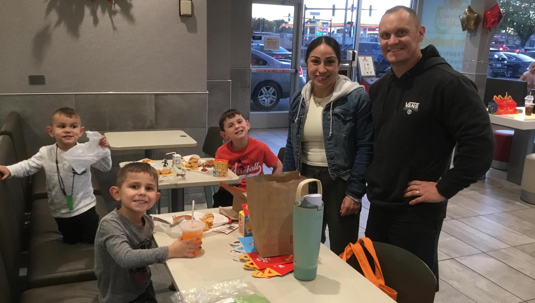 A family gathers at a fast-food restaurant, smiling with children at the table.