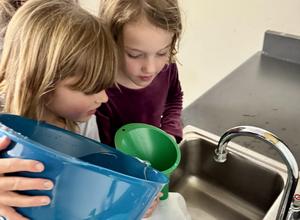 Two girls pour water in a funnel