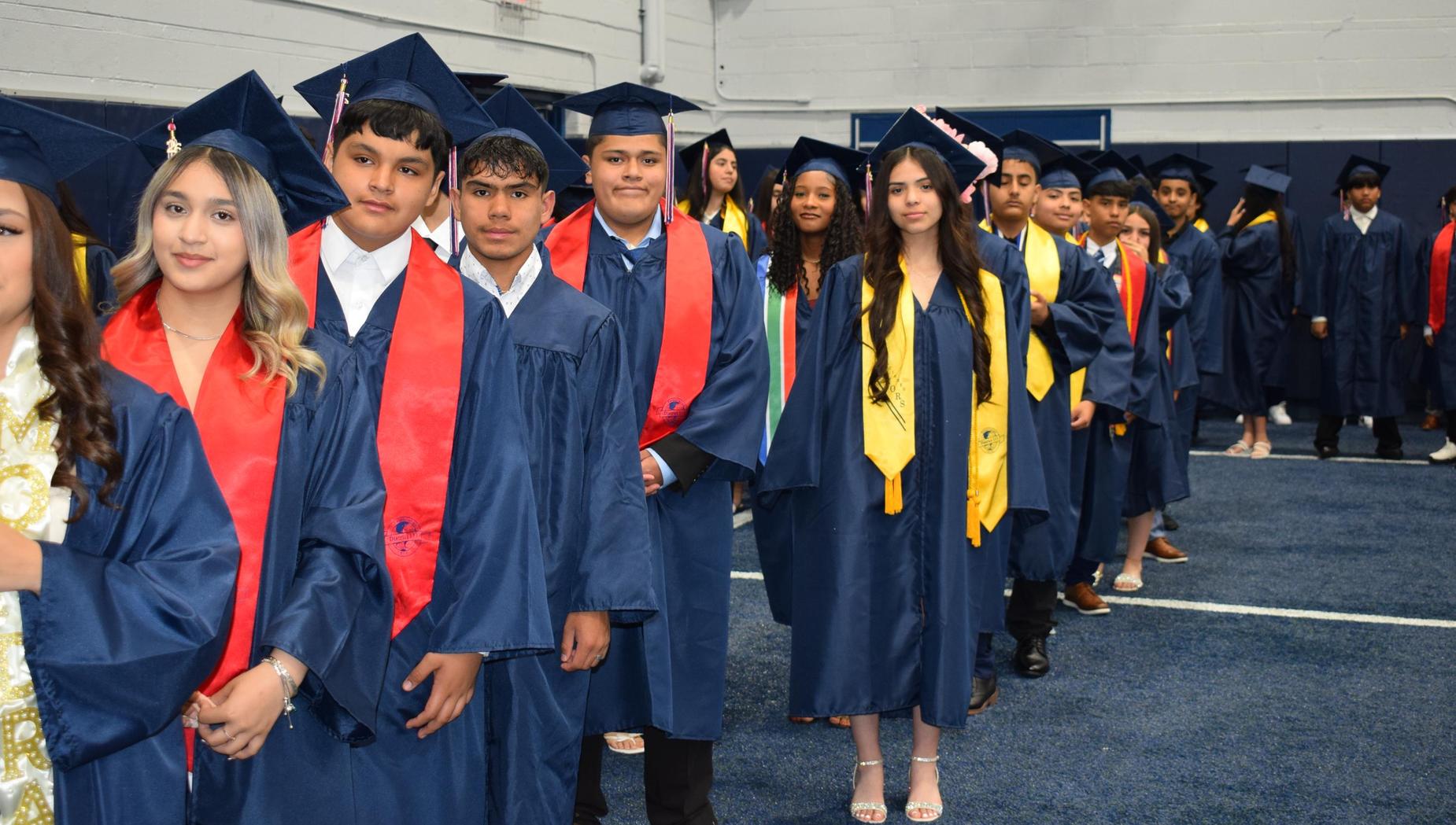 A line of graduates in caps and gowns wait for their turn during a ceremony.