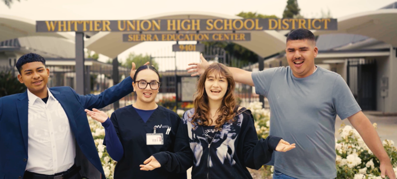 Four USEC students smile and stand in front of the school building.