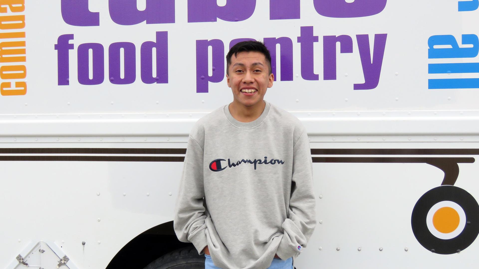 A teen boy stands in front of the Traveling Pantry mobile food truck