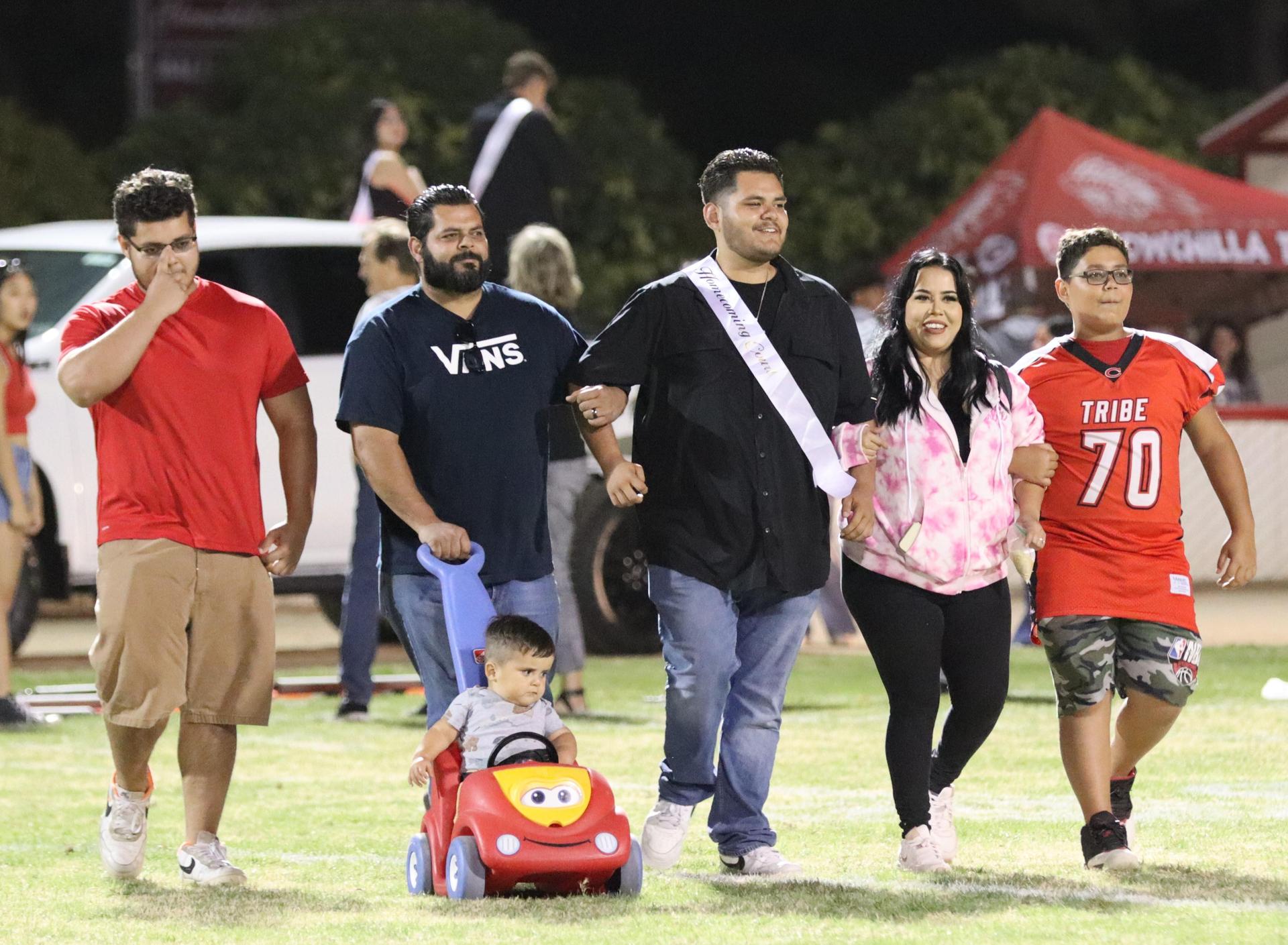 homecoming king and queen candidates walking across the field with their escorts